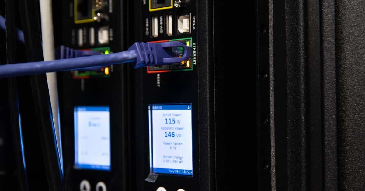 A close-up of a PDU in a server rack with ports, power metric labels, and a connected Ethernet cable.