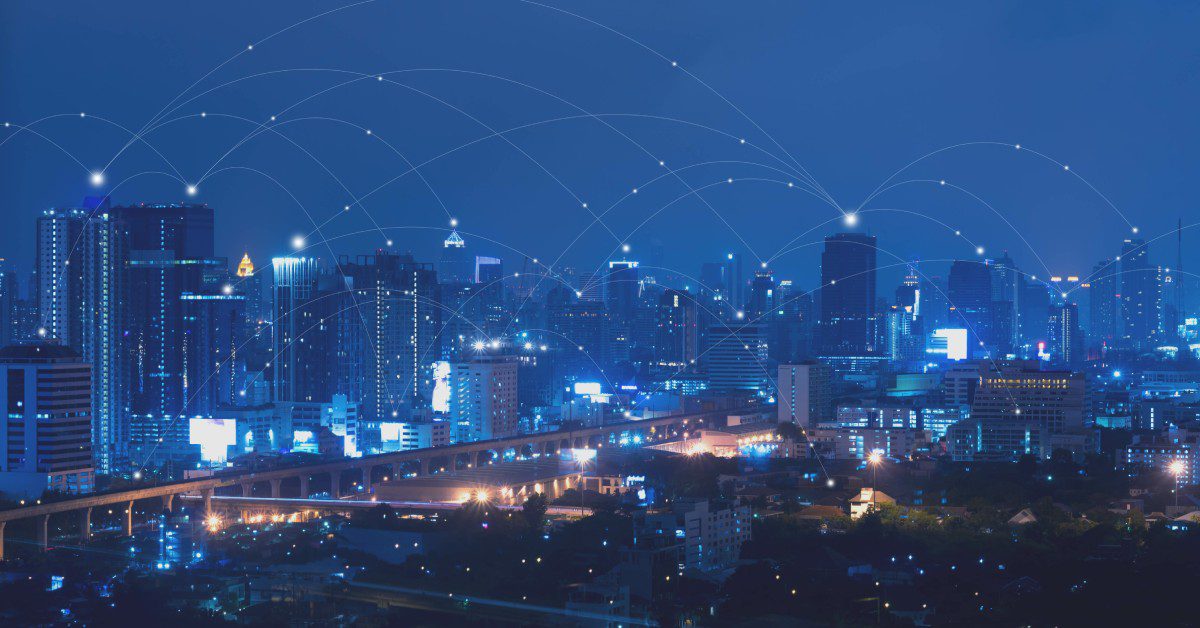 A brightly-lit city at night has lots of blue light lines connecting across the different buildings.